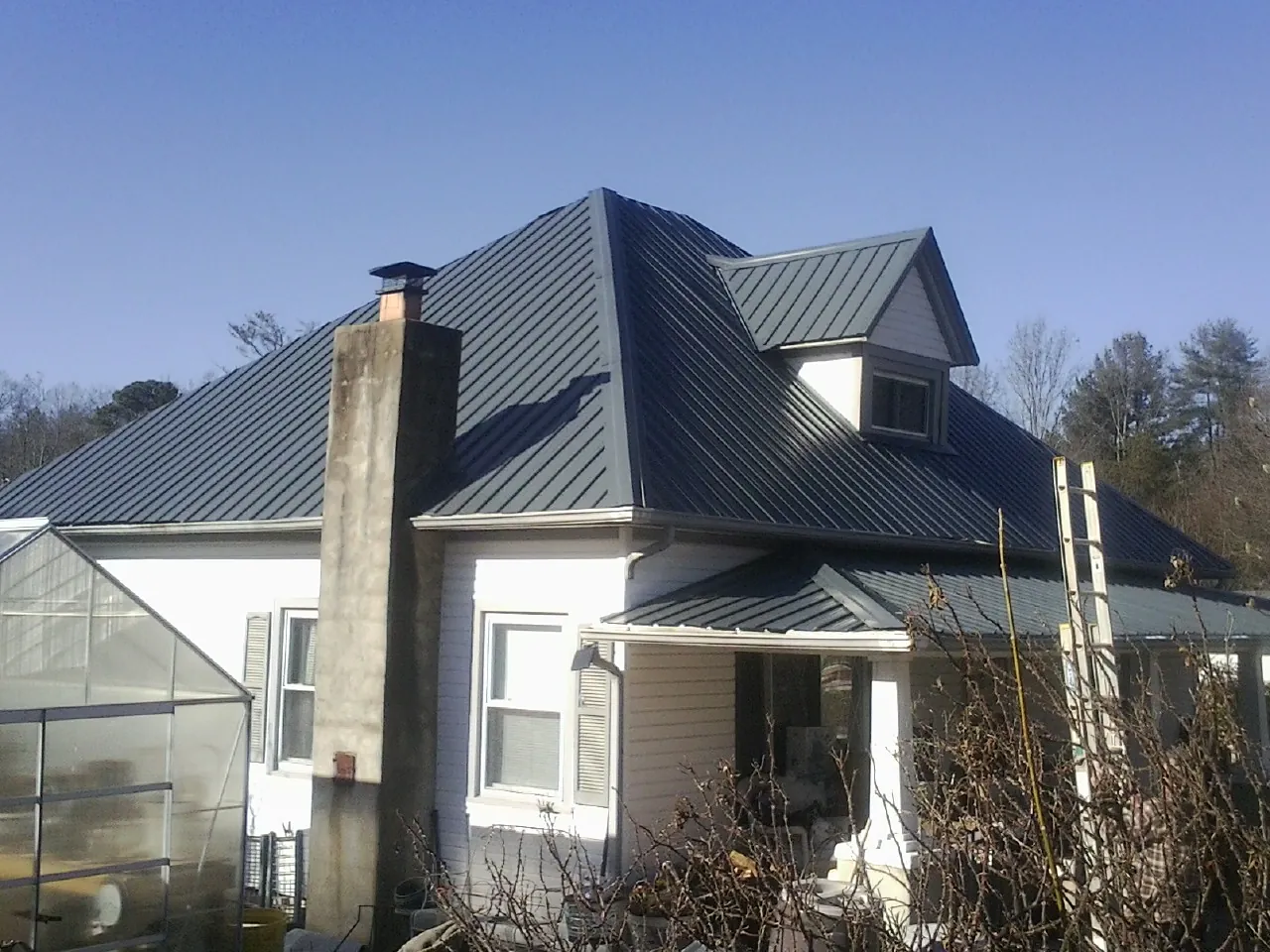 Dark blue standing seam metal roof on a white farmhouse with dormer — Slate & Tile Roof Repair by Roofing Brothers in Great Lakes