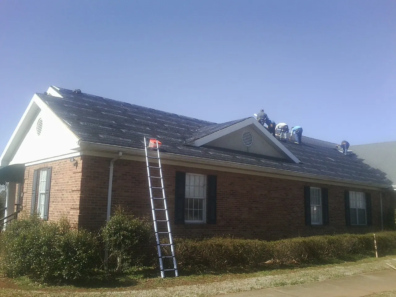 Crew tearing shingles off a brick ranch roof with a ladder set — Emergency Roof Repair work by our crew in Great Lakes