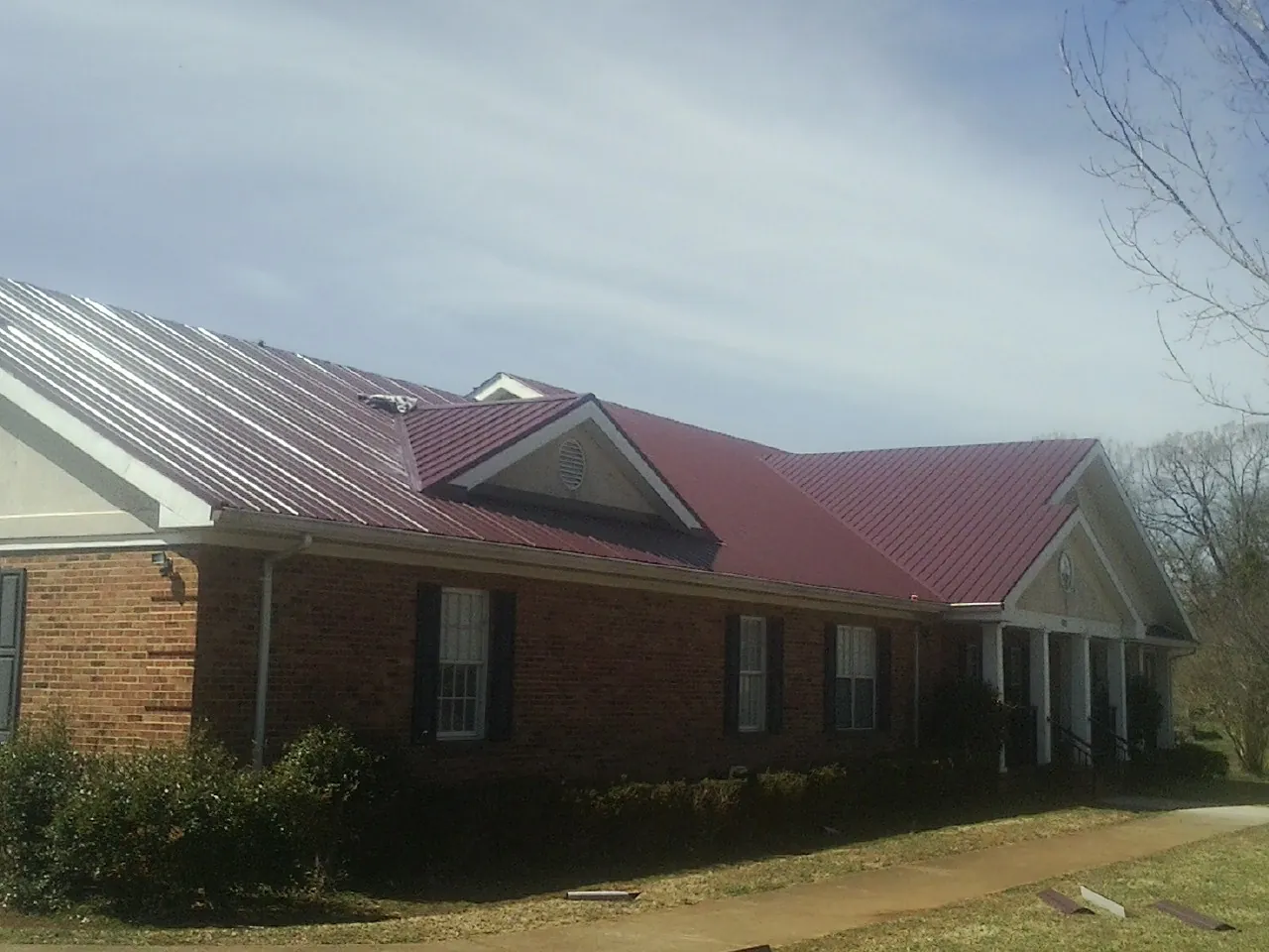 Red metal roof with gabled entries on a long brick building, from a Hail Damage Roof Repair job in Great Lakes