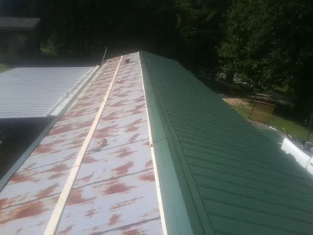 Old rusted panels beside newly installed green metal roofing — Wind Damage Roof Repair by Roofing Brothers in Great Lakes