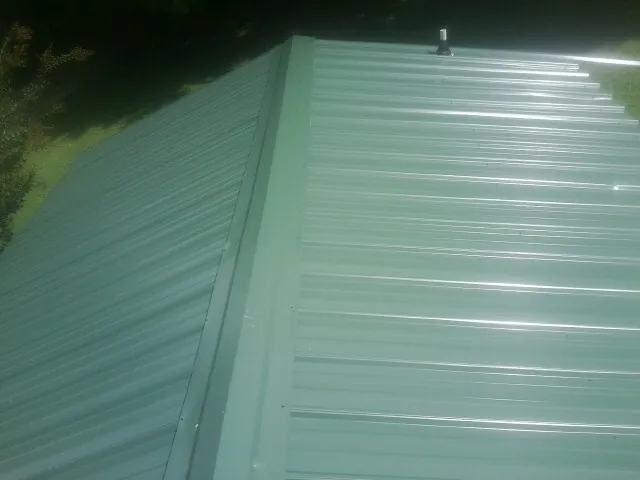 New green metal panels meeting at the ridge of a roof — Flat Roof Repair work by our crew in Great Lakes
