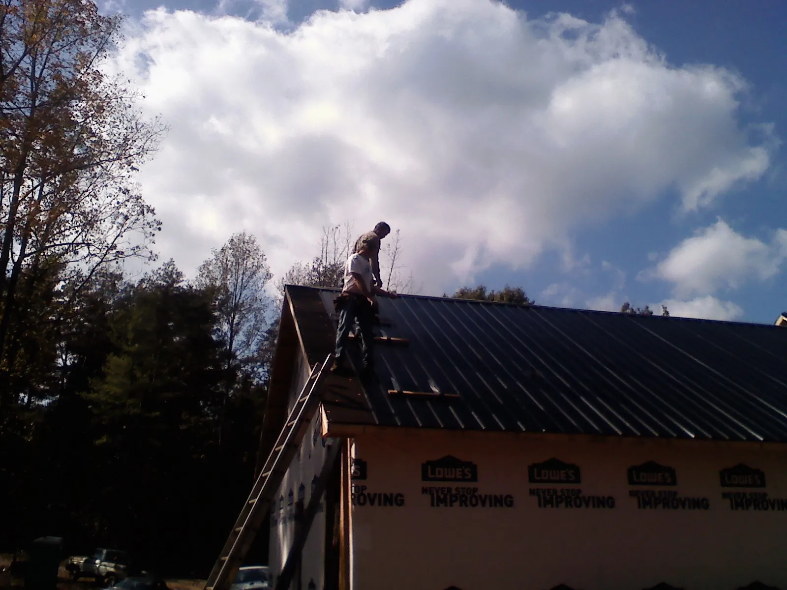 Roofer fastening dark metal panels high against a cloudy sky, from a Roof Inspection job in Great Lakes