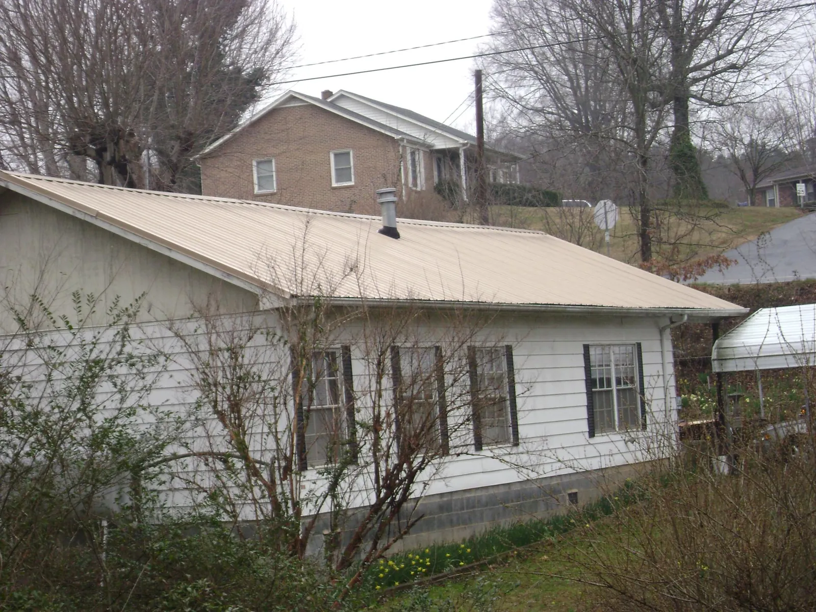 Tan metal roof on a white sided house set into a hillside — Commercial Roofing by Roofing Brothers in Great Lakes