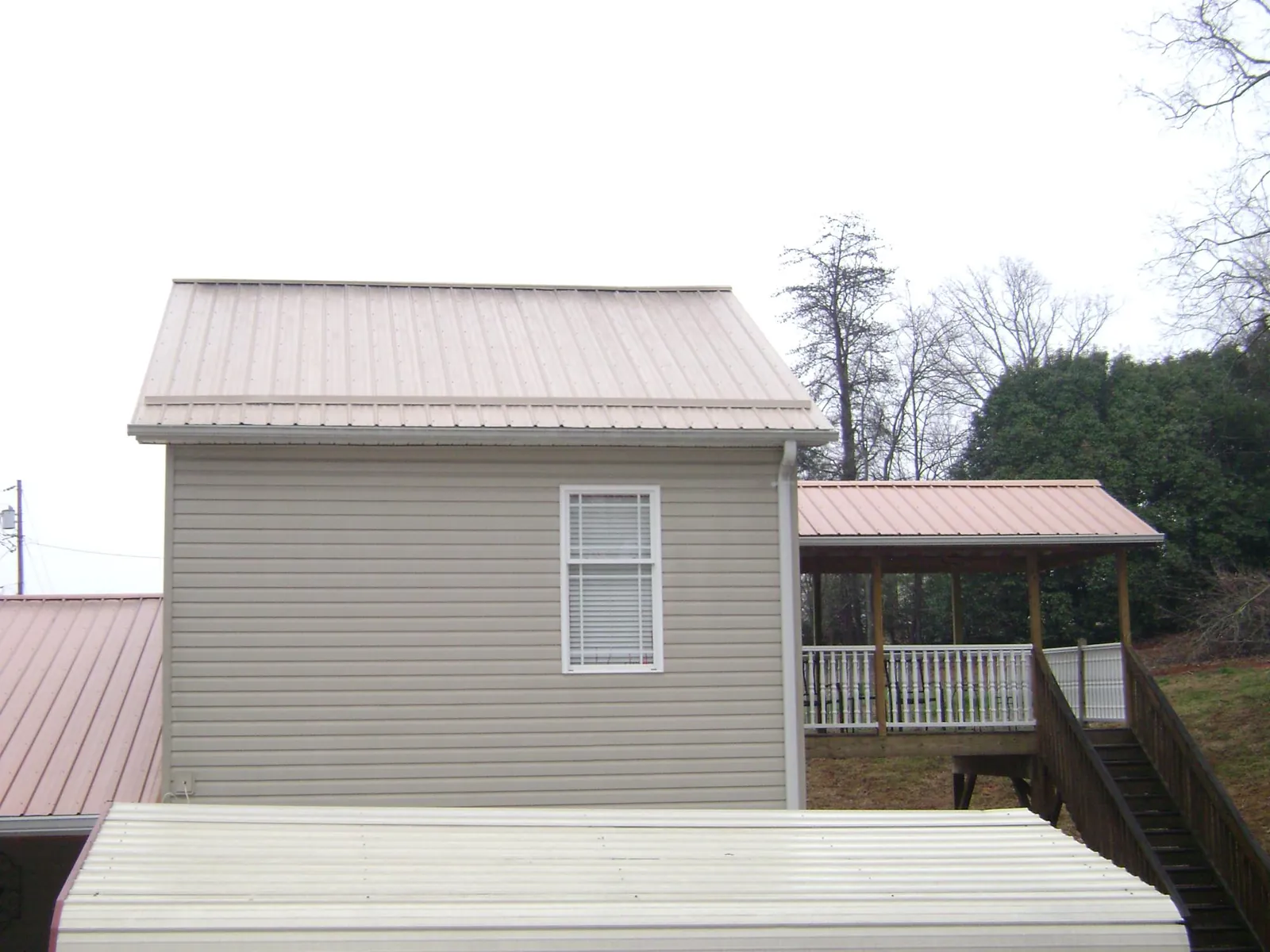 Tan metal roofs on a two story addition and attached porch, from a Roof Replacement job in Great Lakes