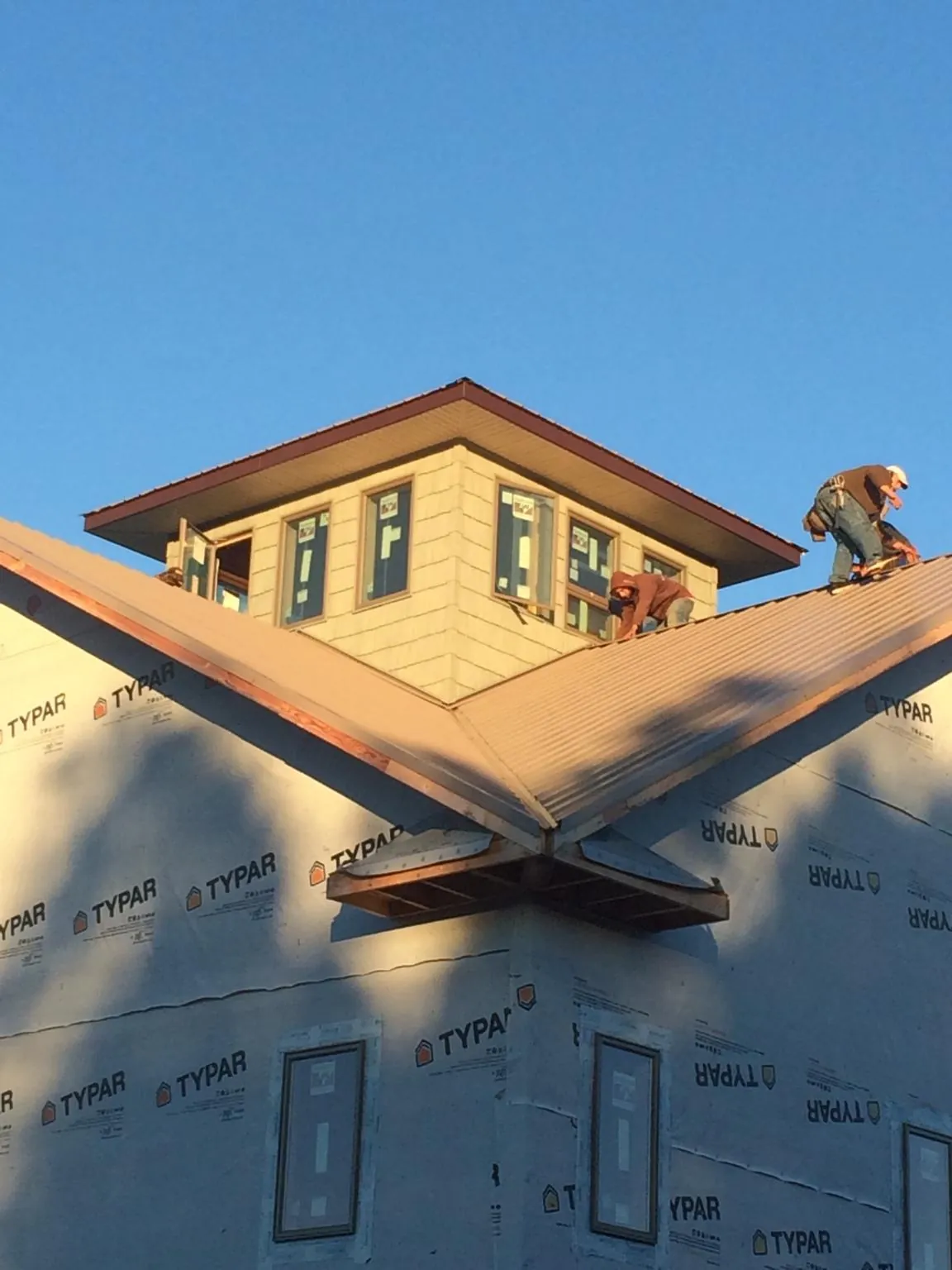 Roofers working around a rooftop cupola on a new metal roof at sunset — Roof Waterproofing in Great Lakes by Roofing Brothers